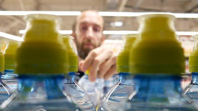 Close-up of many sports plastic bottles of water with yellow caps on a store shelf and a male buyer takes one