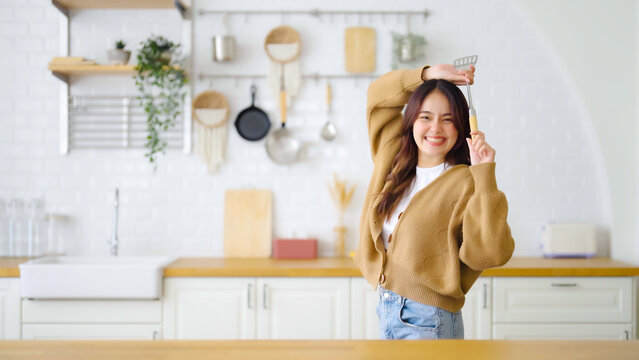 Asian young woman dancing in kitchen room. She happy and relaxing at free time on weekend