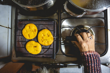 Beautiful hands of elderly latino woman cooking on traditional kitchen stove with gas burners with traditional toaster with 'sopaipillas' (fried pastry) and pots (view from above)