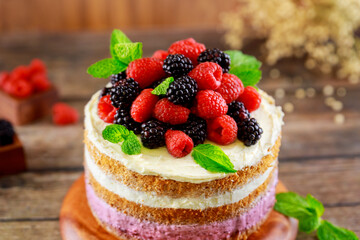 Sponge cake with fresh raspberry and blackberry on wooden table.