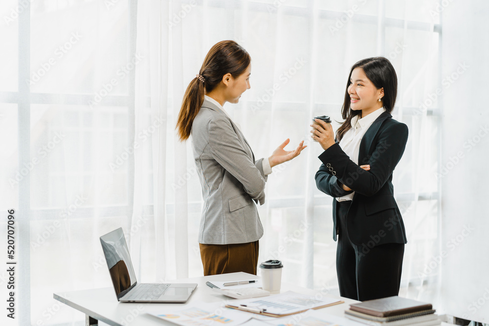 Wall mural two young friends asian business women standing and discussing near the window in the office workpla