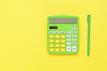 A yellow-green calculator and a green pen on a yellow background. The concept of business and education.