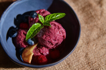 Top view. Delicious healthy raw vegan berry sorbet with ripe juicy fruits and lemon basil leaves in a blue ceramic bowl