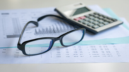 Eyeglasses and calculator on top of financial report and charts. Financial accounting and market trends concept.