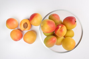 Fresh ripe juicy yellow orange red apricot fruit pile whole cut half slice seed in transparent glass bowl on white background flat lay top view
