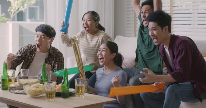 Group of young adult friend man and woman asia people sit at sofa couch joy chanting party fun game world cup live TV at home eat snack bowl drink beer bottle glass jump mad happy win exult face.