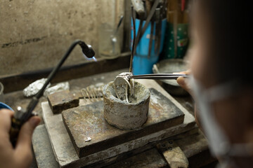 Close-up of a hand of a goldsmith who builds a precious jewel with silver. To make the jewel it takes: precision, craftsmanship and patience. Concept: silver, style, production.