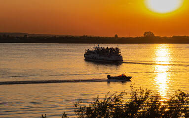 Fototapeta na wymiar ship silhouette at sunset. tourist ship and motor boat at sunset on river horizon natural background