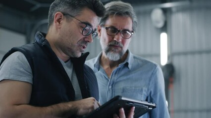 Man mechanic in glasses talking to a client in a car service and showing the results of car diagnostics and repairing on a tablet - Powered by Adobe