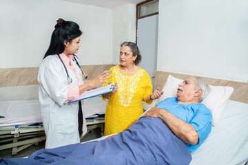 Indian doctor talk to olde senior male patient's wife at clinic or hospital regarding the...
