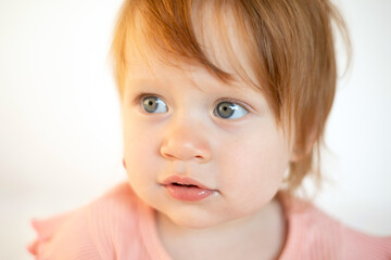 Close up Portrait of a charming cute red-haired baby girl with blue eyes and a birthmark on her cheek. Hemangioma. Light background. Lifestyle