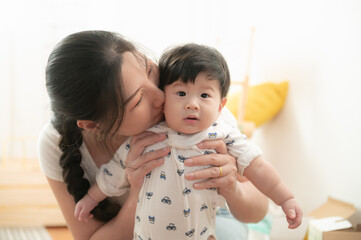 Portrait of Lovely Asian mother holding and kissing adorable baby. Mom with her little baby boy  at...