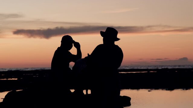 A Man Taking Photo of His Friend at Sunset at The Beach in Silhouette