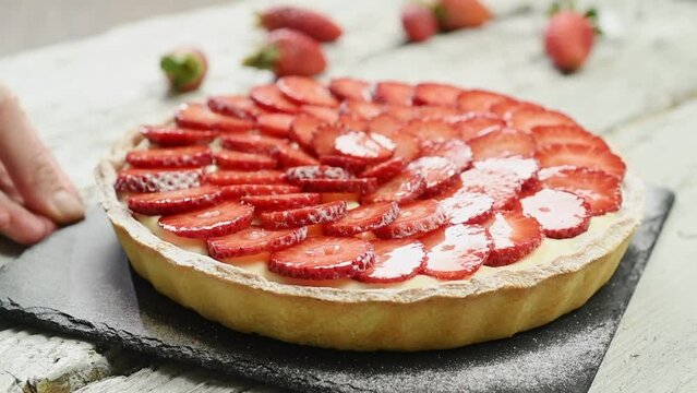 The confectioner serves delicious strawberry tart on the table.
