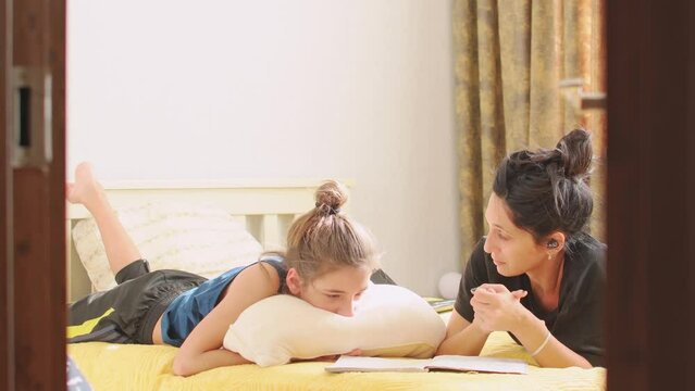 Confused primary child school boy at home hold pillow at difficult homework task while pretty young mother read notebook on bed. Tired frustrated child on pandemic. Slow teenager child development 
