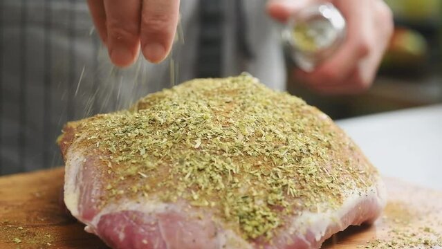 The chef sprinkles raw pork  shoulder with oregano.
