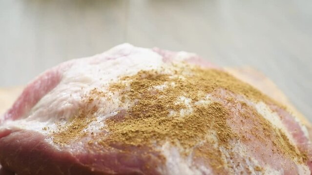 The cook sprinkles raw pork shoulder with cumin.
