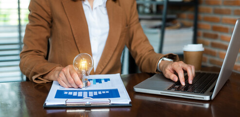 Businesswoman holding and putting lightbulb on coins stack on table for saving energy and money concept..