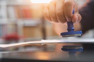 Close up of business person press the seal stamp on paperwork for approval the financial accounting on the desk in the office.