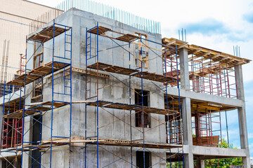 Construction of a new monolithic reinforced concrete house. Scaffolding on the facade of a building under construction. Working at height on a construction site.