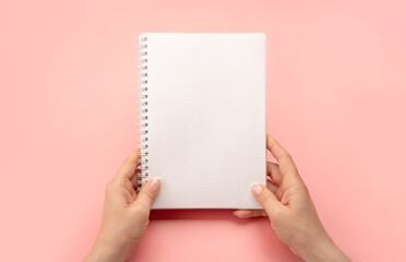 Notepad mockup. female hands holding blank spiral notepad or calendar over pink table background. Hand holding an empty journal binder notepad or notebook. copy space