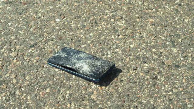 Vehicle tire runs over modern smart phone on paved road, destroying it