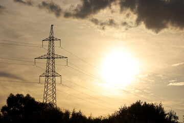 Silhouette of high voltage tower with electrical wires on background of sunset sky and dark clouds....