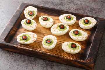 Monster eyes deviled eggs with a avocado and olives for Halloween day on a wooden tray on the...