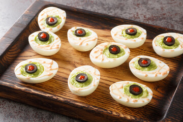 Delicious deviled eggs stuffed with guacamole and olives close-up on a wooden tray on the table. horizontal