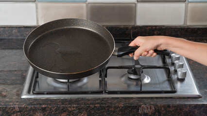 A woman's hand holds a frying pan of oil over a gas stove