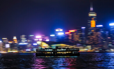 A ferry in Victoria Harbour in Hong Kong with motion blurred background panorama of night skyline...