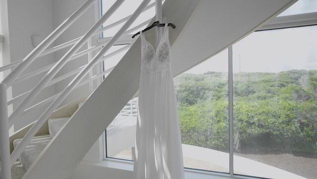 Sunlight shining on bridal dress hanging from stairs. Ascending dynamic gimbal shot