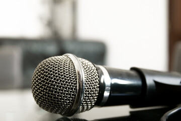 Obraz premium A microphone is laying on a glass table with a bokeh, blurred background. The focus is on the head of the microphone. Black and white. 