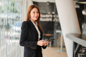 Asian professional businesswoman holding a tablet standing by a glass plate window in the office