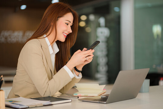 An Asian businesswoman uses a mobile phone while checking email or social media on the Internet. accounting finance concept and calculate with a calculator modern finance and accounting concepts
