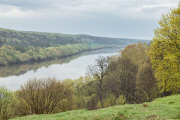 Scenic view on a river with steep banks overgrown with trees and shrubs from a hill in springtime.