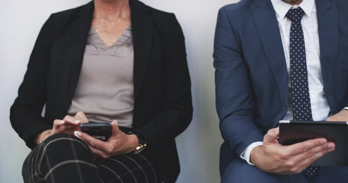 Group of business people sitting in line, waiting for their interview after making the shortlist as a candidate for a vacant job by human resources. Browsing on a tablet and phone while in a row