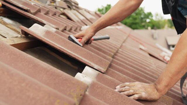 Roofer fixes roof with tiles, medium shot of man at work