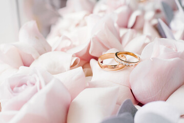 Gold wedding rings lie on delicate pink roses close-up