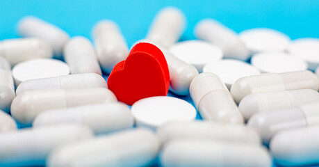 Red pill in the shape of a heart on a background of white pills and a blue background. The concept of love addiction, love drugs, Valentine's Day and depression