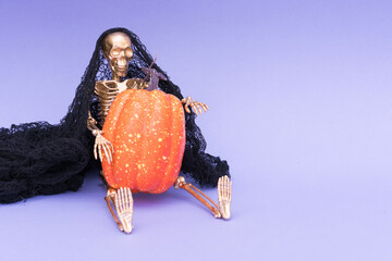 Funny and scary Halloween concept. Golden skeleton holding orange pumpkins against purple background with copy space. Halloween celebration concept