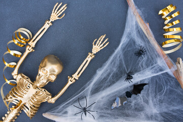 Halloween background. Golden skeleton, cobweb, bats and spiders over dark gray background. Halloween celebration concept. Minimal style