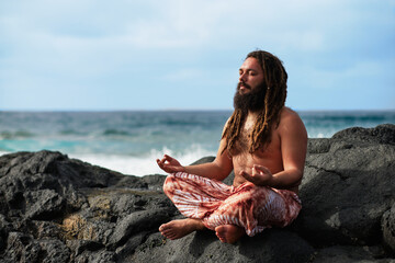 bearded rasta boy meditating by the sea