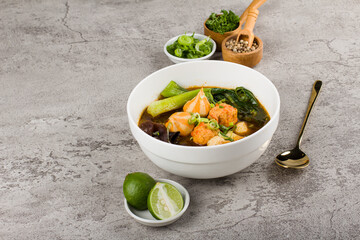 Tom Yam Spicy Thai soup with fish meatball, seafood, coconut milk, mushroom and chili pepper in white bowl on stone background 