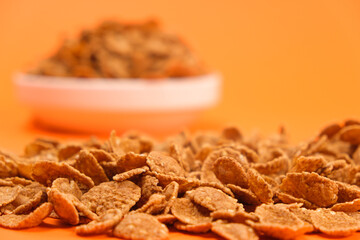 Close-up of wheat flakes on orange background, quick cereal healthy breakfasts.