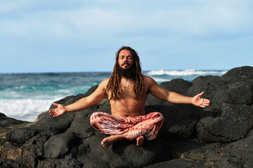 Rasta boy doing yoga with open arms, by the sea.