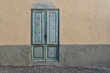 Exterior of an old house with a light blue weathered door on grey and yellow wall, Tuscany, Italy