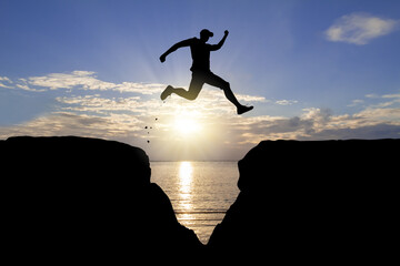 Silhouette of man jumping over the cliff on sunrise background, achievement business concept