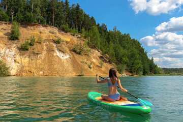 Young beautiful woman in blue bikini is riding on sup board by the Dzerzhinsky quarries.