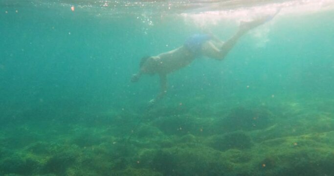 Underwater footage scene of young man snorkeling, swimming with fins, searching and hunting fish with spear in the sea. Turquoise color of the water. Summer holidays activity.